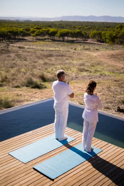 Casal praticando ioga na beira da piscina — Fotografia de Stock