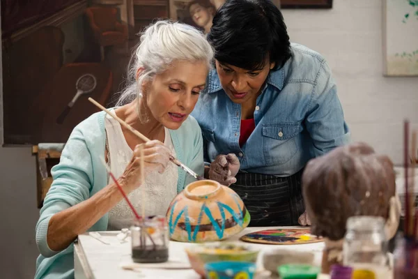 Mujer ayudando a la mujer mayor en tazón de pintura — Foto de Stock