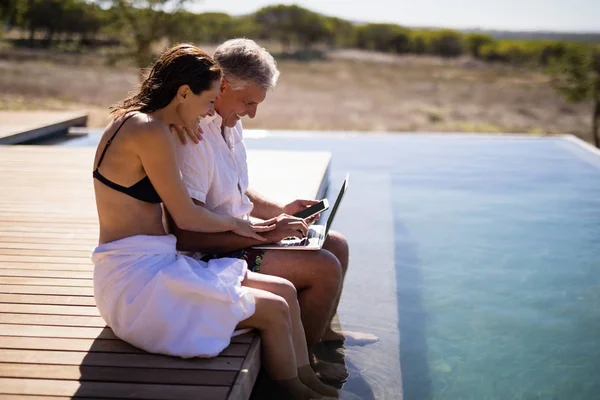 Couple using laptop near poolside — Stock Photo, Image