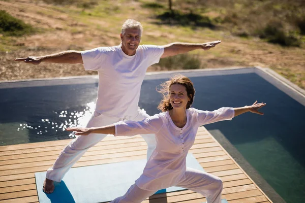 Casal praticando ioga na beira da piscina — Fotografia de Stock
