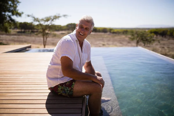 Uomo sorridente seduto vicino al lato piscina — Foto Stock