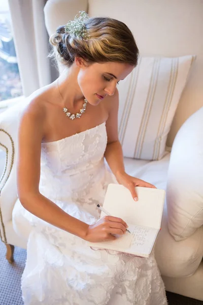 Bruid schrijven in dagboek zittend op fauteuil — Stockfoto