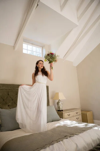 Nevěsta drží kytici stoje na posteli — Stock fotografie