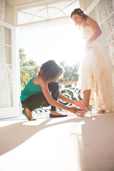 Kosmetikerin zieht Braut zu Hause Sandalen an — Stockfoto