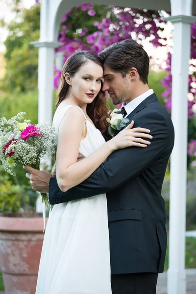 Bride embracing bridegroom in park — Stock Photo, Image