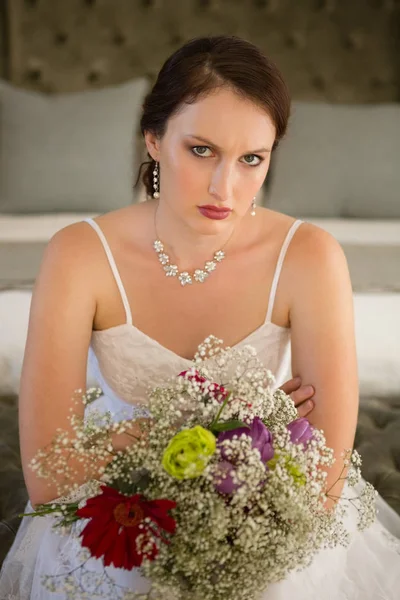 Sad bride with bouquet sitting on bed — Stock Photo, Image