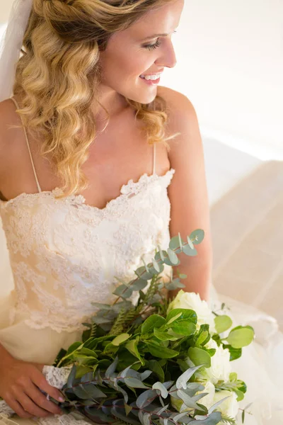 Bride holding bouquet while sitting on bed — Stock Photo, Image