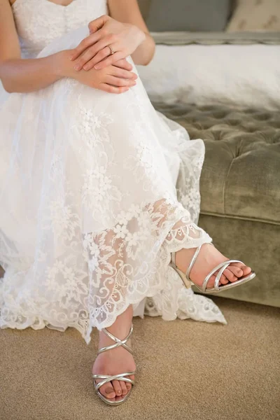 Невеста в серебряных сандалиях сидит на кровати — стоковое фото