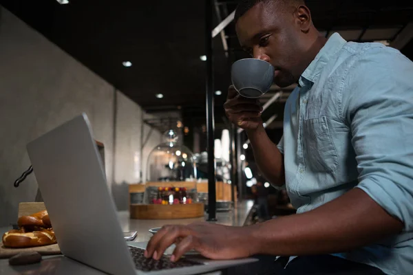 Человек пьет кофе во время использования ноутбука — стоковое фото