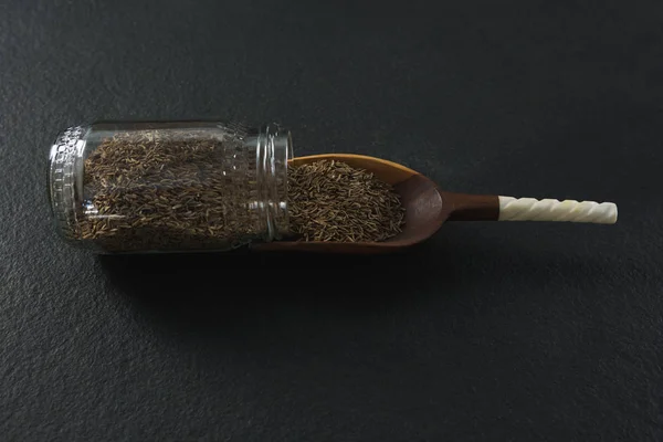 Cumin spilling out of jar into scoop — Stock Photo, Image