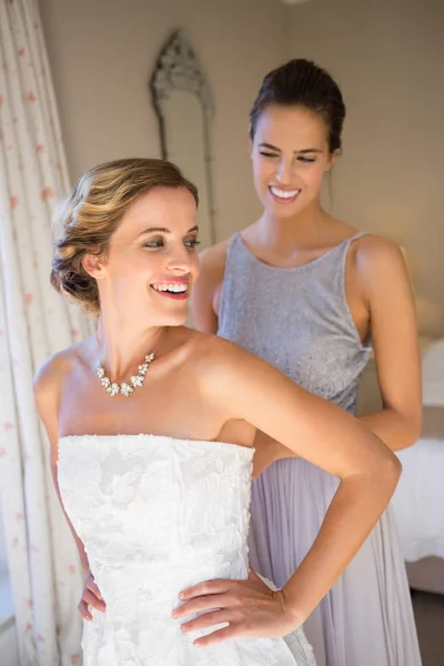 Bridesmaid adjusting bride wedding dress in room — Stock Photo, Image