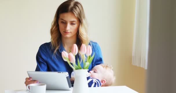 Madre utilizzando tablet digitale durante l'alimentazione del suo bambino — Video Stock