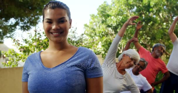 Trainer and seniors exercising in background — Stock Video