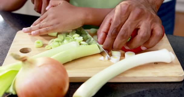 Отец помогает сыну резать овощи — стоковое видео