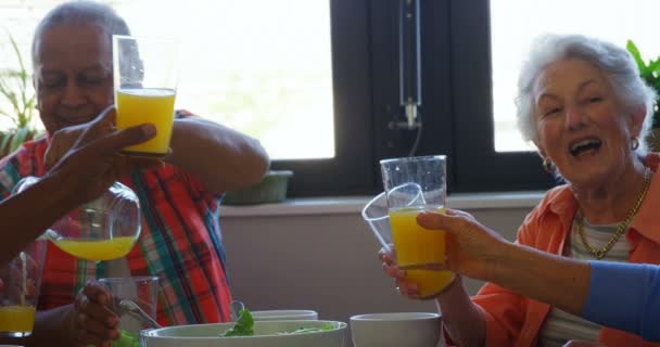 Amigos mayores brindando vasos de jugo en la mesa de comedor — Vídeos de Stock