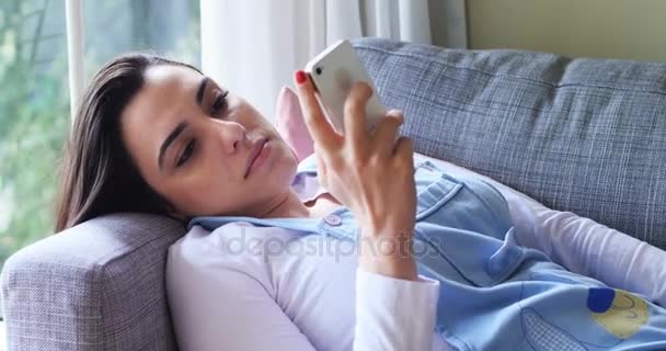 Mujer usando el teléfono móvil mientras se relaja en el sofá — Vídeo de stock