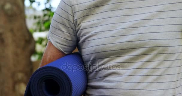 Lachende senior man met yoga mat in de tuin — Stockvideo