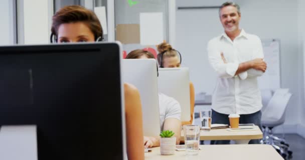 Exécutif souriant debout avec les bras croisés tandis que des collègues parlent sur casque 4k — Video