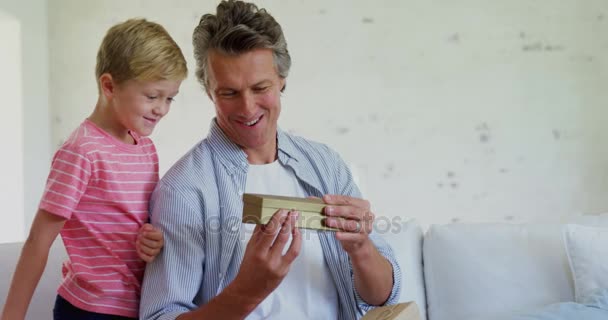 Son giving gift box to father in living room — Stock Video