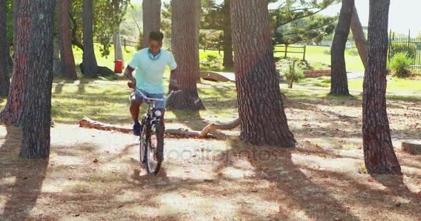 Человек в наушниках катается на велосипеде в парке 4k — стоковое видео
