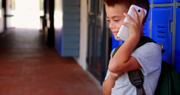 Счастливый школьник разговаривает по мобильному телефону в коридоре — стоковое видео