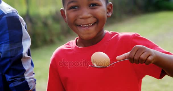Счастливый мальчик держит яйцо и ложку на заднем дворе — стоковое видео