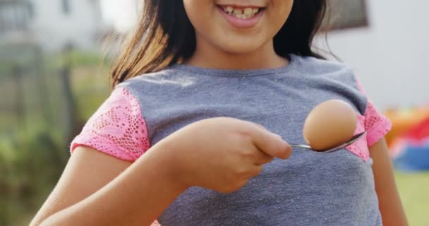 Girl holding egg and spoon in backyard — Stock Video