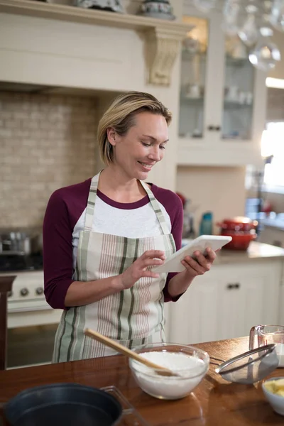 Woman using tablet while preparing cookies — Stock Photo, Image