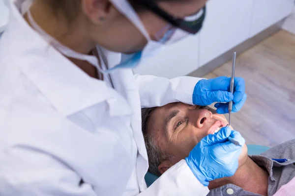 Zahnarzt hält Werkzeug in der Hand, während er Mann untersucht — Stockfoto