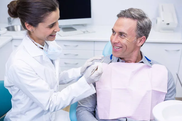 Dentist holding tool while looking at man — Stock Photo, Image
