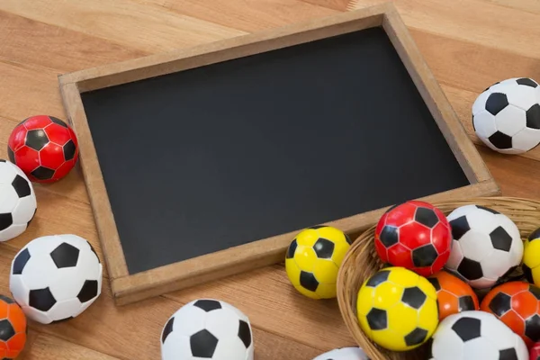 Pelotas de fútbol de colores y pizarra en la mesa de madera — Foto de Stock