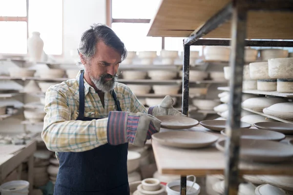 Male potter placing plate on shelf — Stock Photo, Image