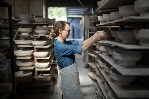 Female potter placing bowl in shelf — Stock Photo, Image