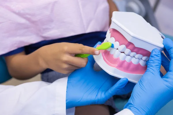 Dentista enseñando a niño cepillarse los dientes en la clínica —  Fotos de Stock