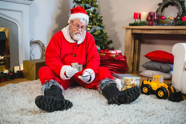 Santa claus sitter på golvet och räknar pengar — Stockfoto