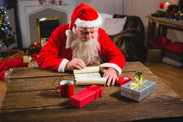 Weihnachtsmann liest Schriftrolle im Wohnzimmer — Stockfoto