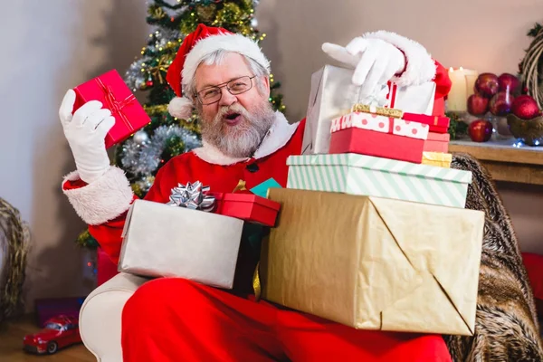Santa hediyeler yığını ile kanepede oturan — Stok fotoğraf