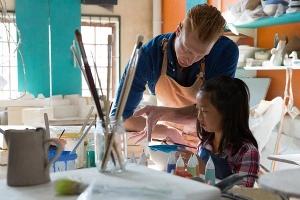 Male potter assisting girl to paint bowl — Stock Photo, Image