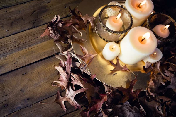 Rozsvícené svíčky a suché listí na stůl — Stock fotografie