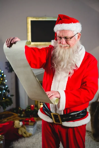 Weihnachtsmann liest Schriftrolle im Wohnzimmer — Stockfoto