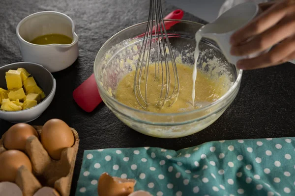 Женщина добавляет молоко к взбитым яйцам в миску — стоковое фото
