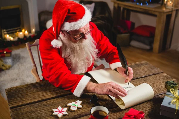 Santa Claus writing on scroll in living room — Stock Photo, Image