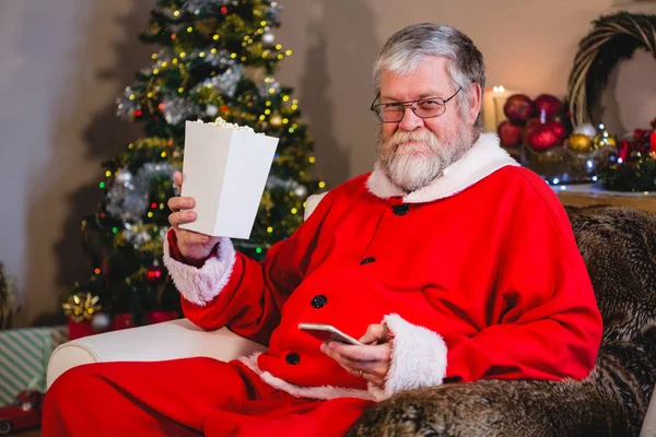 Santa Claus using mobile while having popcorn — Stock Photo, Image