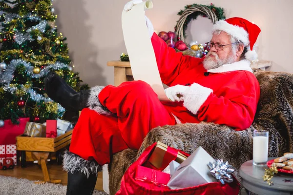 Weihnachtsmann liest Schriftrolle im Wohnzimmer — Stockfoto