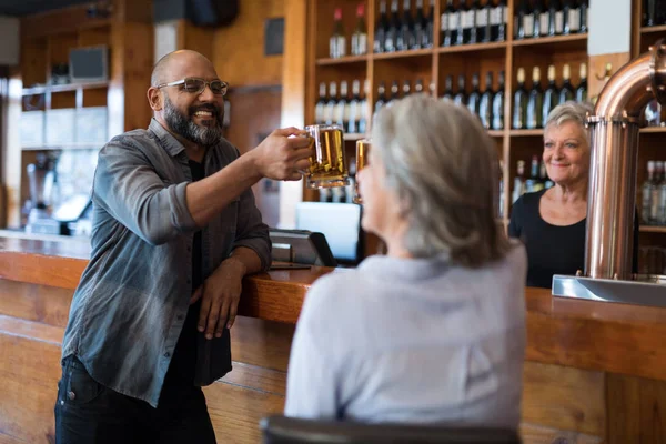 Friends toasting glass of beer at counter — Stock Photo, Image