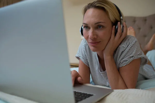 Mujer usando el ordenador portátil mientras escucha música — Foto de Stock