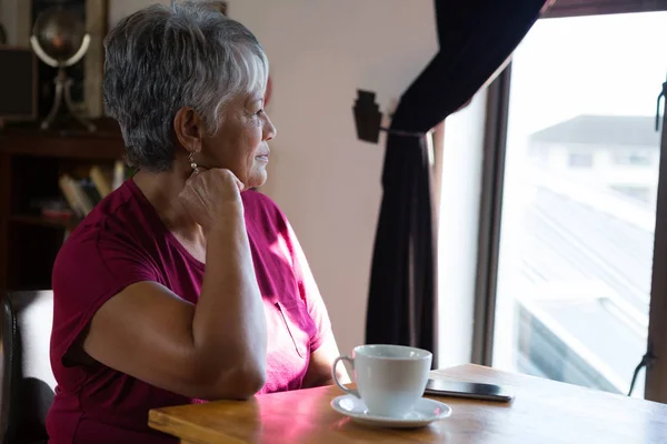 Äldre kvinna som tittar genom fönstret — Stockfoto