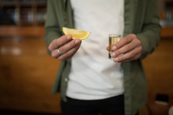 Uomo in possesso di shot di tequila e limone cuneo — Foto Stock