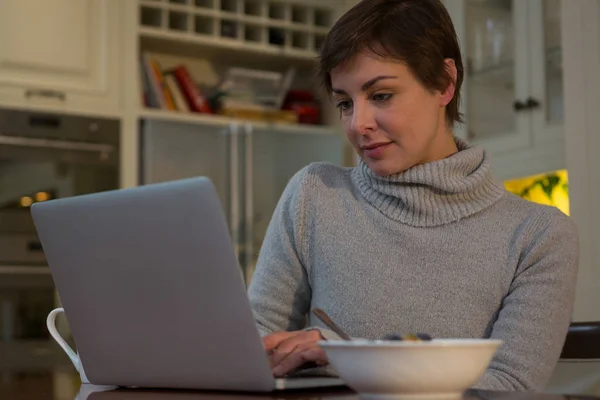 Mulher tomando café da manhã ao usar laptop — Fotografia de Stock