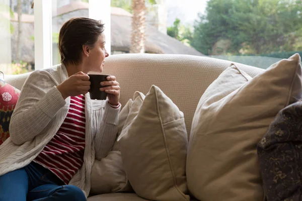 Женщина смотрит в окно, когда пьет кофе — стоковое фото